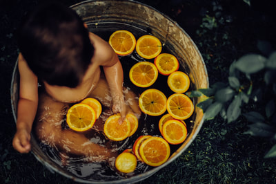 this little boy is taking a bath in oranges in a summer mini session in suffolk county 
