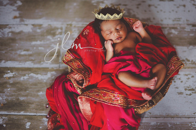 a newborn indian baby on a rustic floormat wearing her moms sari from her wedding day