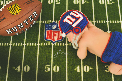 a newborn baby boy wearing a new york giants football helmet on an nfl rug 