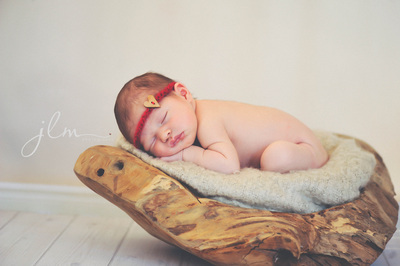 a newborn baby in a rustic piece of wood wearing a red valentines day headband 