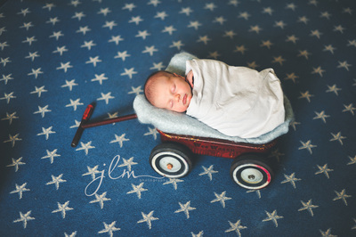 a newborn baby in a rustic red wagon on a rug with stars 