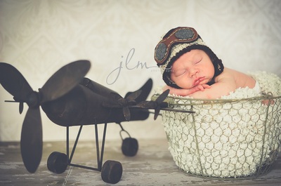 a newborn baby in a rustic wire basket wearing an aviator hat and vintage airplane 