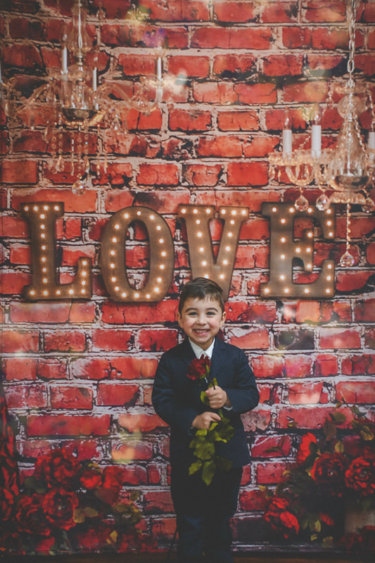 this little boy is holding a rose at a valentines day mini session at a studio on long island 